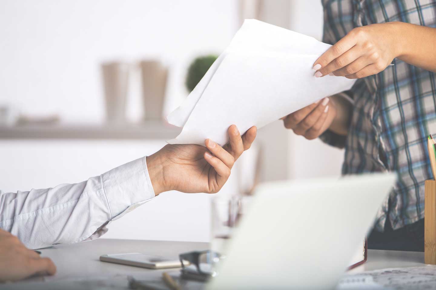 People handing a document to each other with a laptop